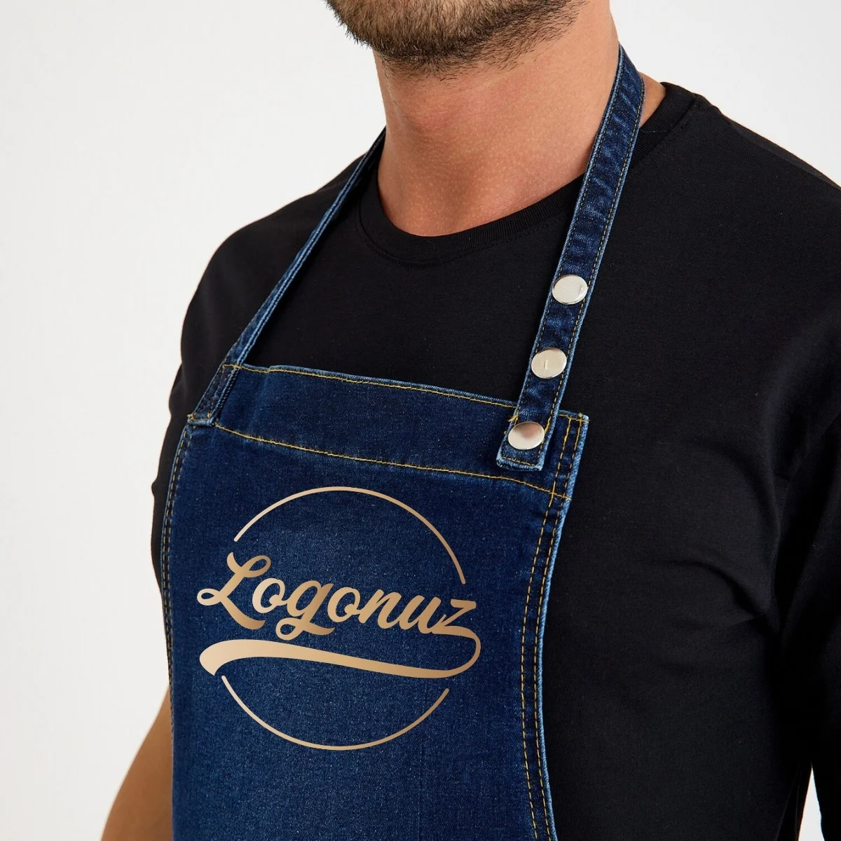 Kot denim önlük üzerindeki gold logo baskı ve metal düğmeli boyun askısı yakın çekim
